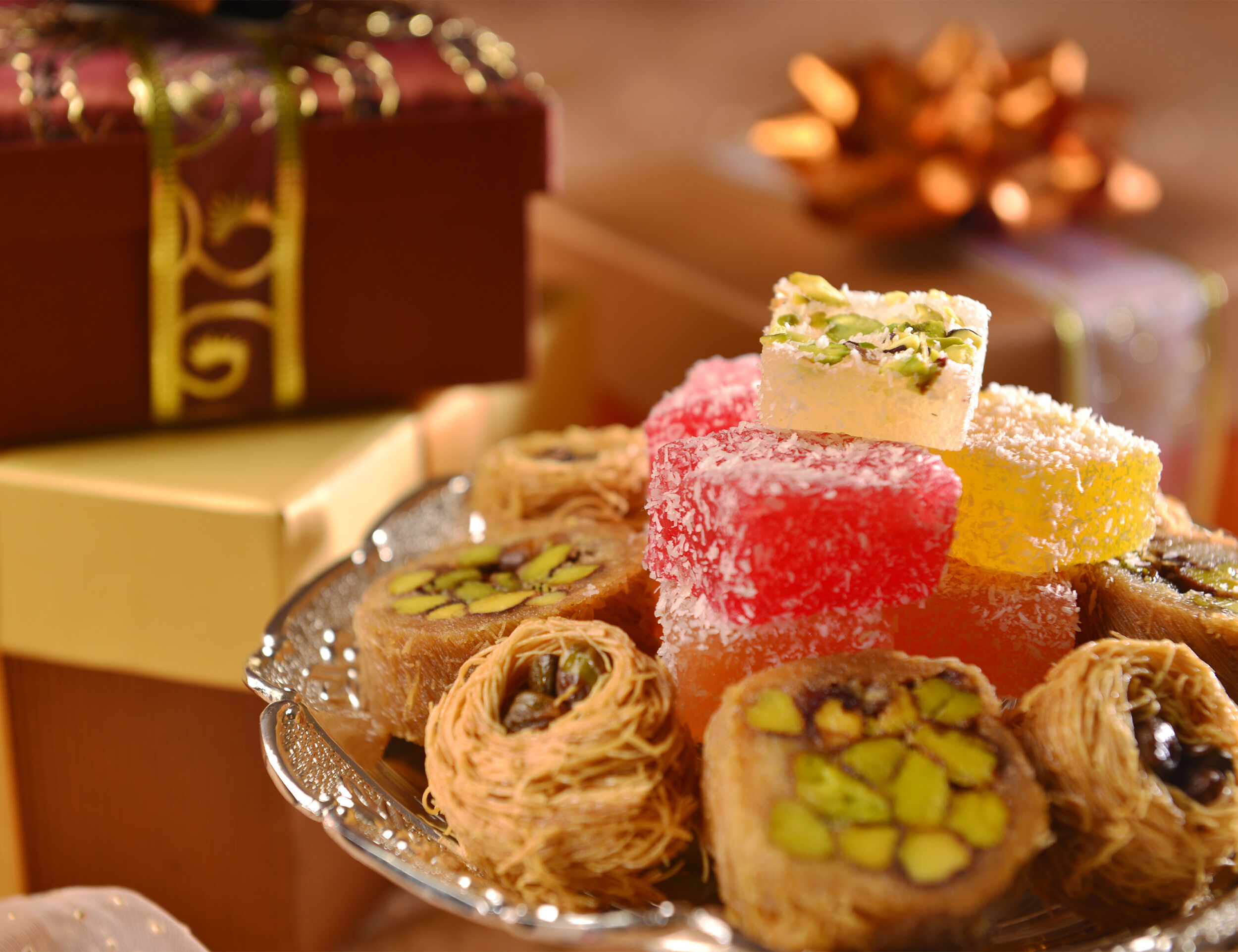 A platter of traditional Eid sweets, including baklava and Turkish delight, with festive gift boxes in the background